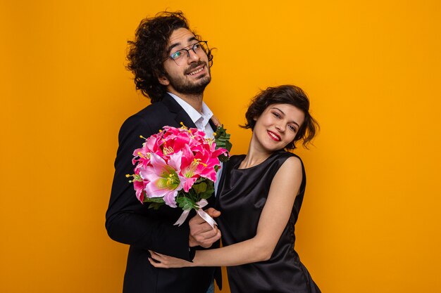 Joven hermosa pareja hombre feliz con ramo de flores y mujer sonriendo alegremente abrazando feliz enamorado celebrando San Valentín