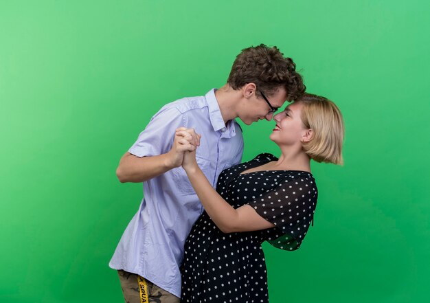 Joven hermosa pareja hombre y mujer bailando juntos felices y alegres sobre la pared verde