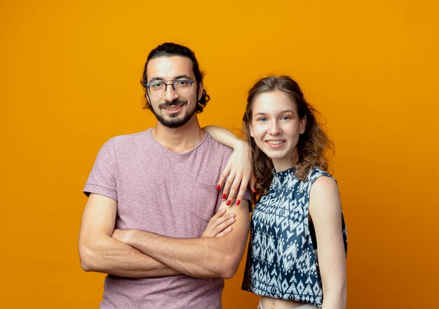 Joven hermosa pareja hombre y mujer felices enamorados mirando a la cámara de pie sobre fondo naranja