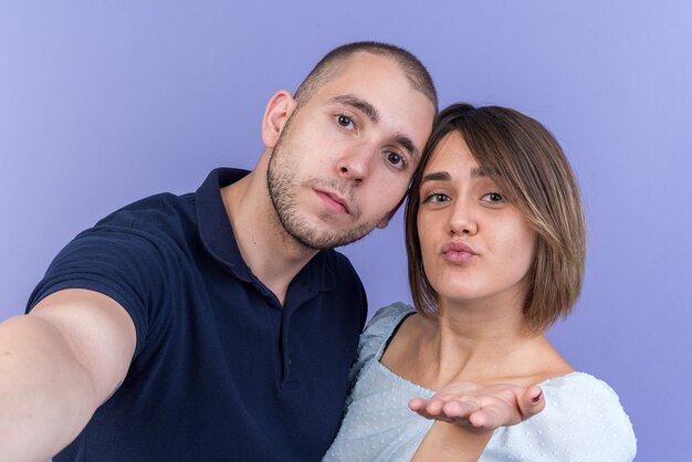 Joven hermosa pareja hombre y mujer feliz y positivo que sopla un beso con la mano delante de su rostro de pie sobre la pared azul