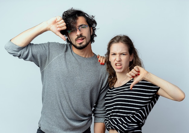 Joven hermosa pareja hombre y mujeres disgustados mostrando los pulgares hacia abajo sobre la pared blanca