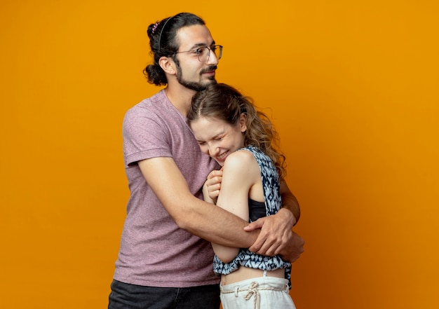 Foto gratuita joven hermosa pareja hombre y mujeres felices enamorados abrazándose juntos de pie sobre fondo naranja