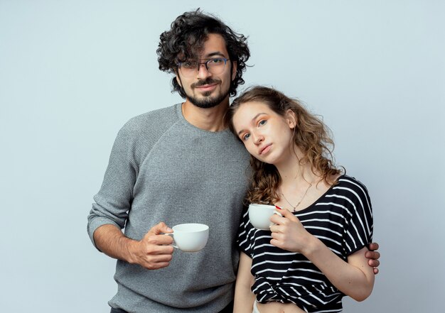 Joven hermosa pareja hombre y mujeres felices enamorados sosteniendo tazas de café sintiendo emociones positivas sobre fondo blanco.