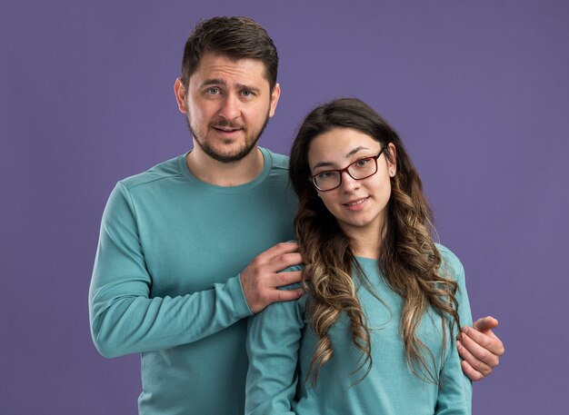 Joven hermosa pareja en ropa casual azul feliz y alegre hombre y mujer feliz en el amor sonriendo celebrando el día de San Valentín de pie sobre la pared púrpura