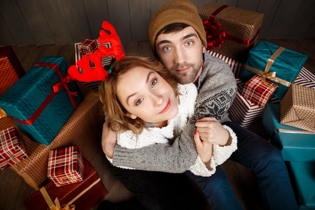 Joven hermosa pareja sonriente abrazando sentado entre cajas de regalo de Navidad.