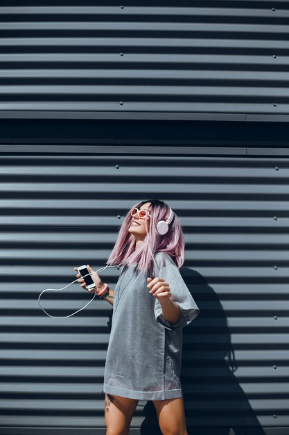 La joven hermosa usa un teléfono inteligente en la calle, navega por Internet y escucha música.