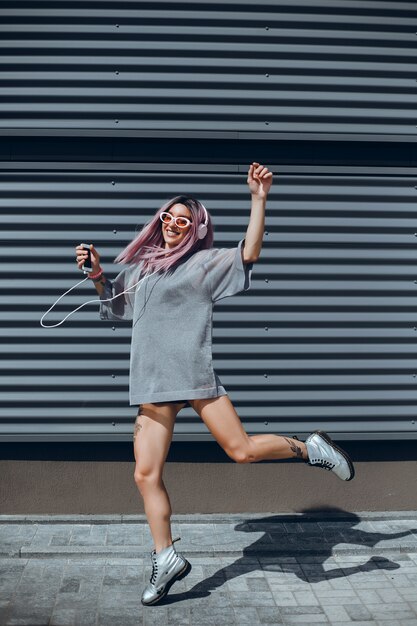 La joven hermosa usa un teléfono inteligente en la calle, navega por Internet y escucha música.