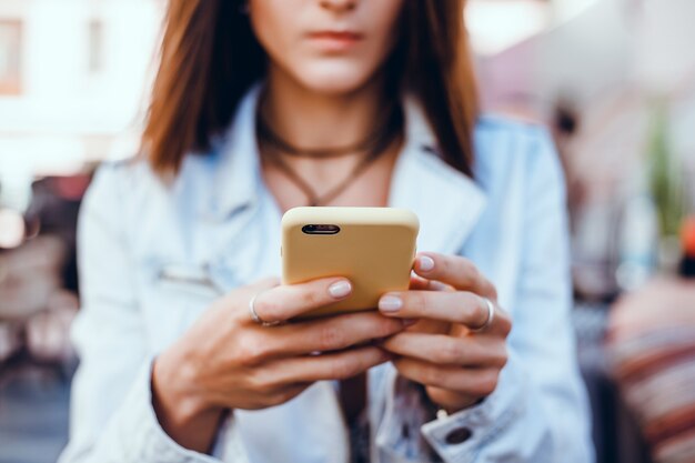 Joven hermosa usa un teléfono inteligente en la calle, navegando por internet