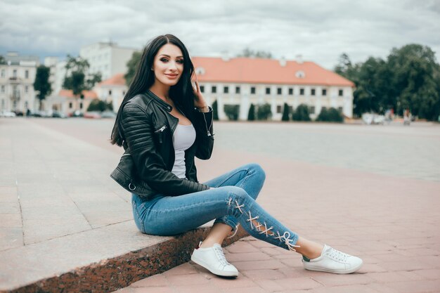 Joven hermosa usa un teléfono inteligente en la calle, navegando por internet