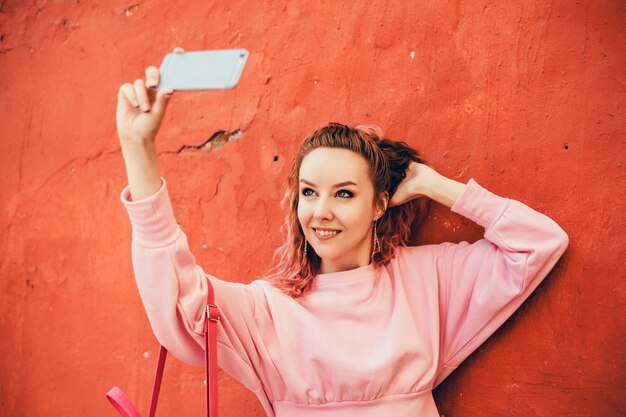 Joven hermosa usa un teléfono inteligente en la calle, navegando por internet