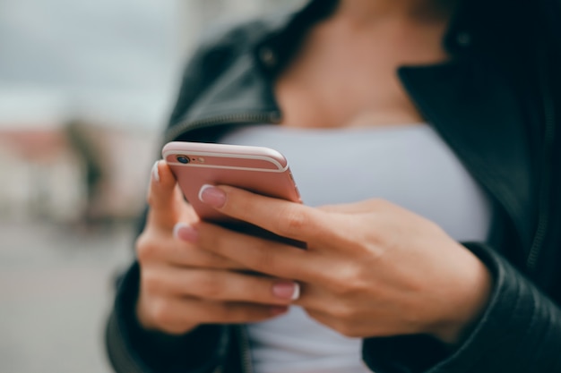 Joven hermosa usa un teléfono inteligente en la calle, navegando por internet