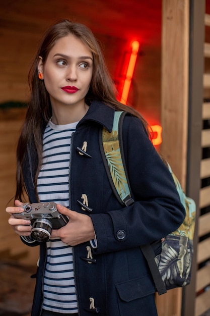 Una joven hipster feliz sostiene una cámara de fotos retro. Divertirse en la ciudad con cámara, foto de viaje del fotógrafo.