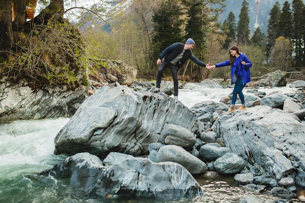 Foto gratuita joven hipster hermosa pareja de enamorados caminando sobre una roca en el río en el bosque de invierno