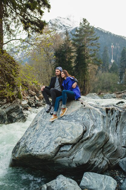 Joven hipster hermosa pareja de enamorados caminando sobre una roca en el río en el bosque de invierno