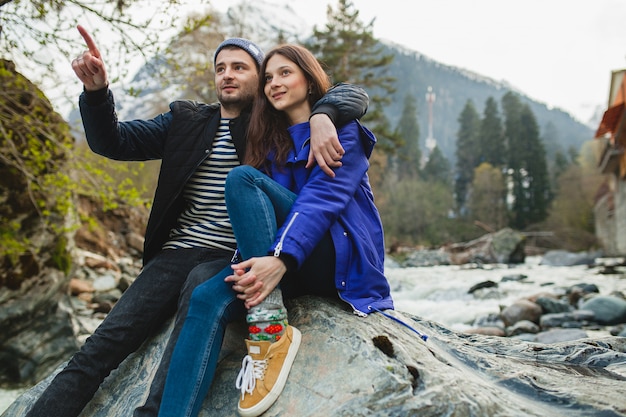 Joven hipster hermosa pareja de enamorados caminando sobre una roca en el río en el bosque de invierno