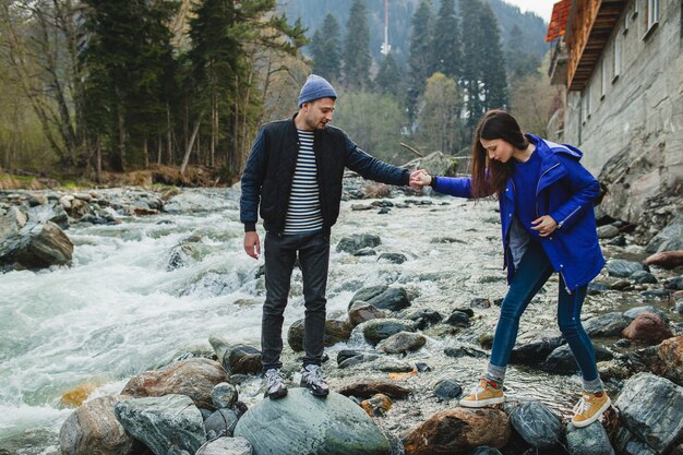 Joven hipster hermosa pareja de enamorados caminando sobre una roca en el río en el bosque de invierno