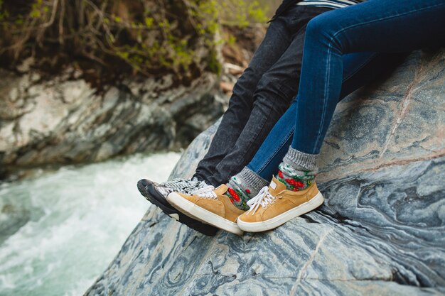 Joven hipster hermosa pareja de enamorados sentados en una roca en el río en el bosque de invierno