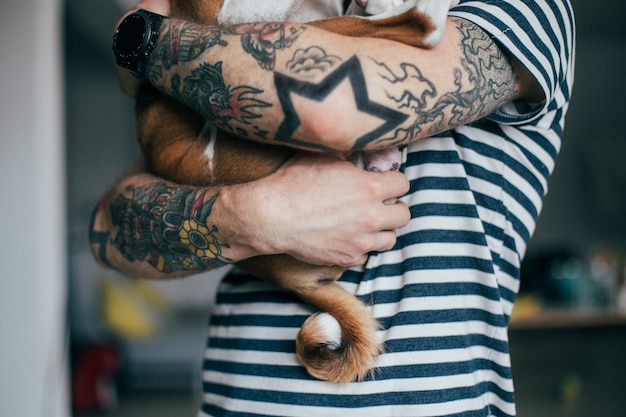 Joven hipster de moda con tatuajes loco pelo rizado abraza a su pequeño mejor amigo