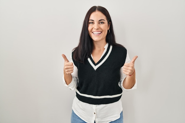 Joven hispana parada sobre un aislado signo de éxito de fondo haciendo un gesto positivo con la mano, pulgares arriba sonriendo y feliz. expresión alegre y gesto ganador.