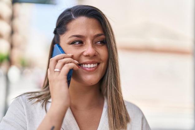 Joven hispana sonriendo confiada hablando por el teléfono inteligente en la calle