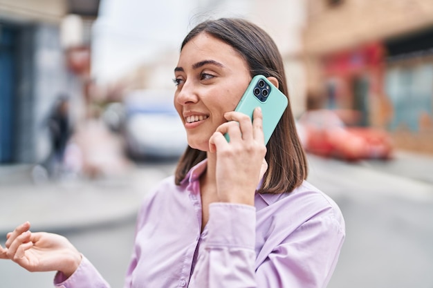 Joven hispana sonriendo confiada hablando por el teléfono inteligente en la calle