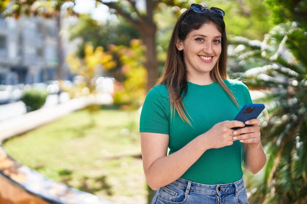 Foto gratuita joven hispana sonriendo confiada usando un teléfono inteligente en el parque