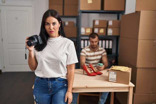 Foto gratuita joven hispana sosteniendo una cámara trabajando en una pequeña empresa de comercio electrónico con actitud de pensamiento y expresión sobria que parece segura de sí misma