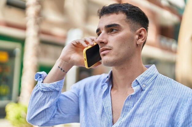 Joven hispano hablando por teléfono inteligente con expresión seria en la calle