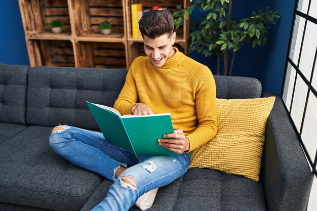 Joven hispano leyendo un libro sentado en un sofá en casa