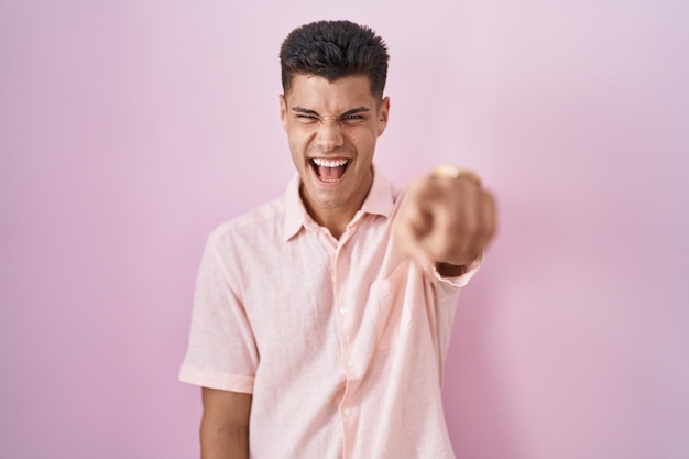 Foto gratuita joven hispano parado sobre un fondo rosado señalando disgustado y frustrado a la cámara enojado y furioso contigo