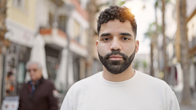 Joven hispano de pie con expresión seria en la calle