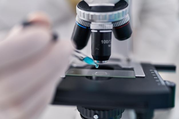 Joven hispano con uniforme de científico usando microscopio en el laboratorio