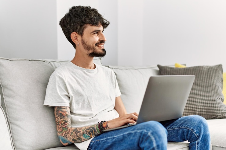 Foto gratuito joven hispano usando una laptop sentada en el sofá de casa
