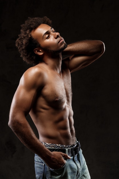 Joven hombre africano deportivo posando sobre pared negra.