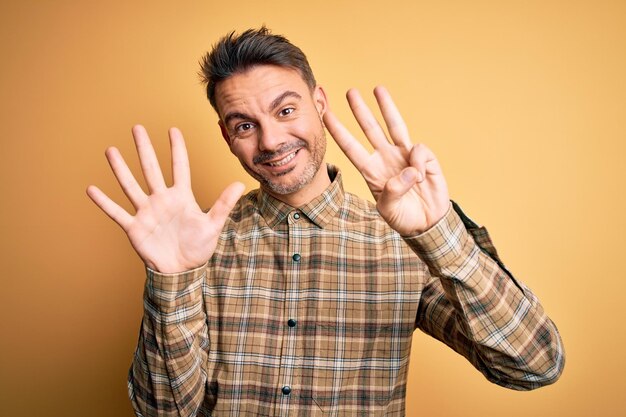 Joven hombre apuesto con pantalones casual parado sobre un fondo amarillo aislado que aparece y señala con los dedos número ocho mientras sonríe confiado y feliz