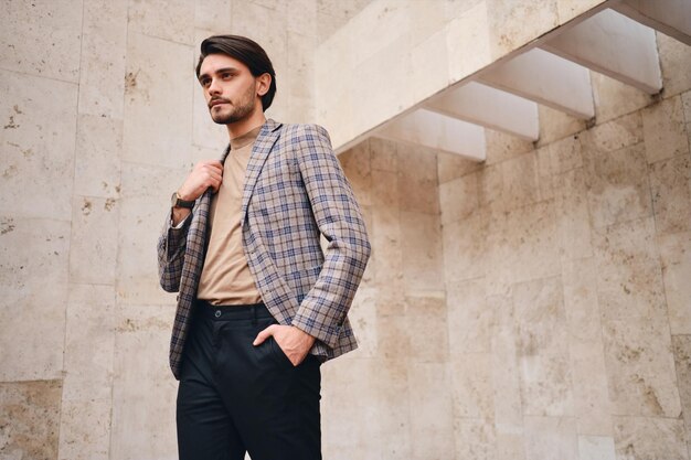 Joven hombre atractivo y elegante con chaqueta a cuadros mirando pensativamente hacia otro lado al aire libre