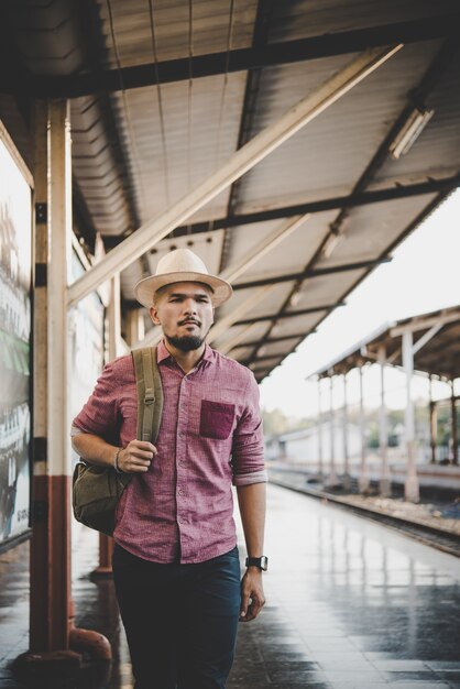 Joven hombre hipster caminando por la estación de tren. Hombre esperando el tren en la plataforma. Concepto de viaje.