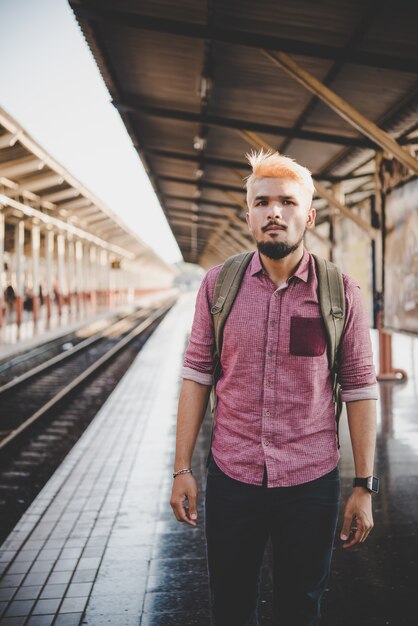 Joven hombre hipster caminando por la estación de tren. Hombre esperando el tren en la plataforma. Concepto de viaje.