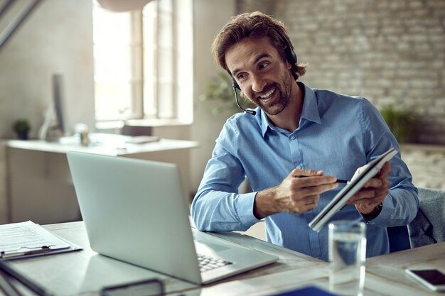 Joven hombre de negocios feliz que usa una computadora portátil mientras tiene una reunión en línea desde su oficina