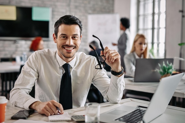 Joven hombre de negocios feliz trabajando en la oficina y mirando a la cámara Hay gente en el fondo