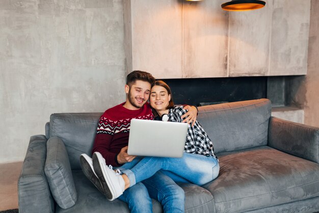 Joven inconformista sonriente hombre y mujer sentados en casa en invierno, sosteniendo una computadora portátil, pareja de ocio juntos, estudiando en línea, autónomo, feliz, citas, velada romántica