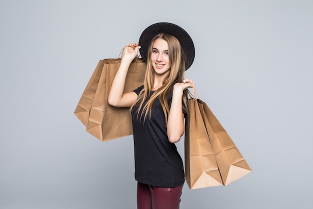 Joven inconformista vestida con camiseta negra y pantalones de cuero sosteniendo bolsas de compras artesanales en blanco con asas aisladas en blanco