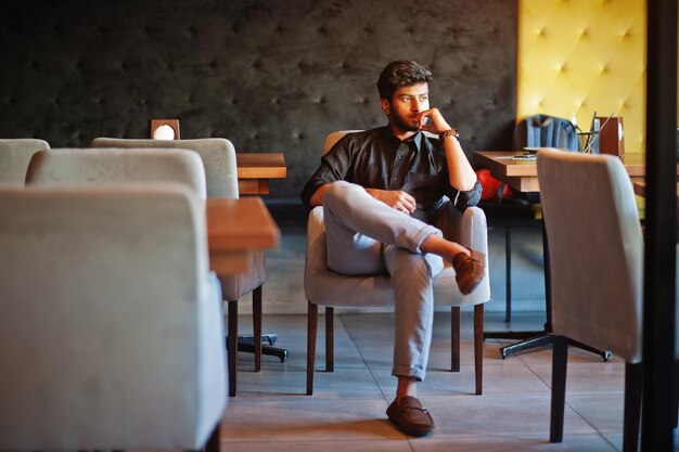 Foto gratuita joven indio confiado con camisa negra sentado en el café