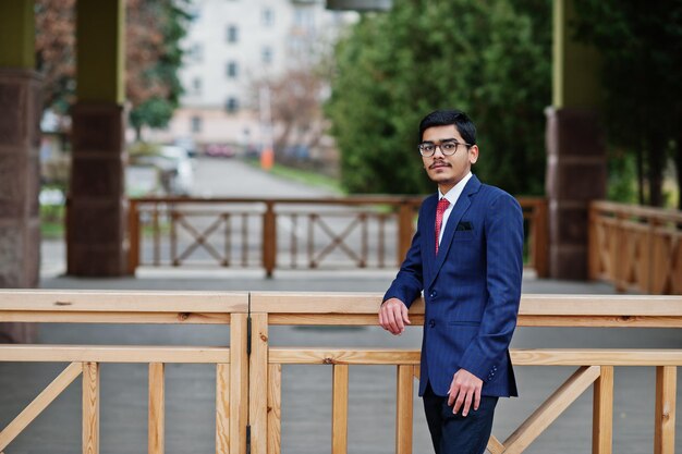 Joven indio con gafas puestas en traje con corbata roja posado al aire libre