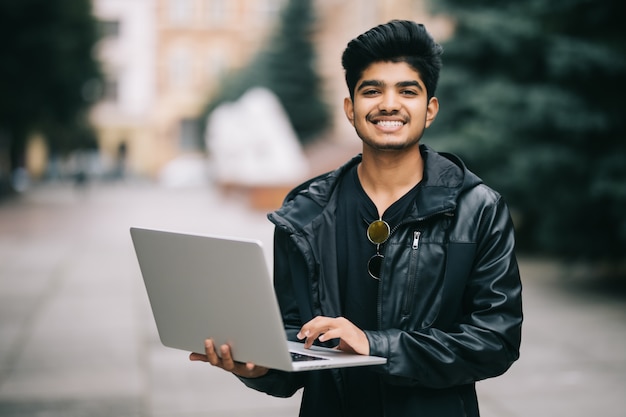 Joven indio parado al aire libre con la computadora portátil en el frente