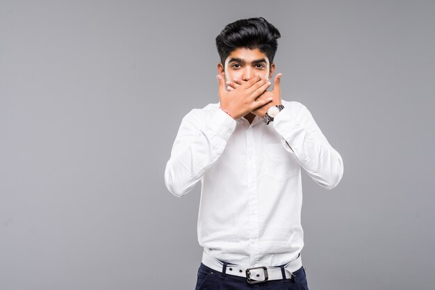 Joven indio vistiendo camisa elegante de pie sobre la pared blanca aislada sorprendido cubriendo la boca con las manos por error Concepto secreto