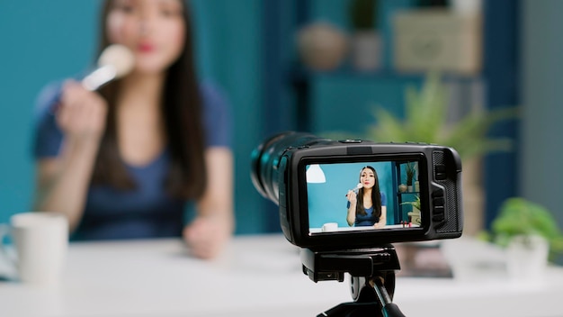 Joven influenciador revisando el pincel de maquillaje en video, grabando vlog en línea en cámara profesional. Blogger de belleza haciendo recomendaciones de productos con cosméticos glam, filmando en estudio. De cerca.