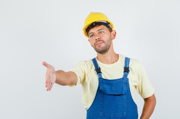 Joven ingeniero estirando la mano para agitar en vista frontal uniforme.