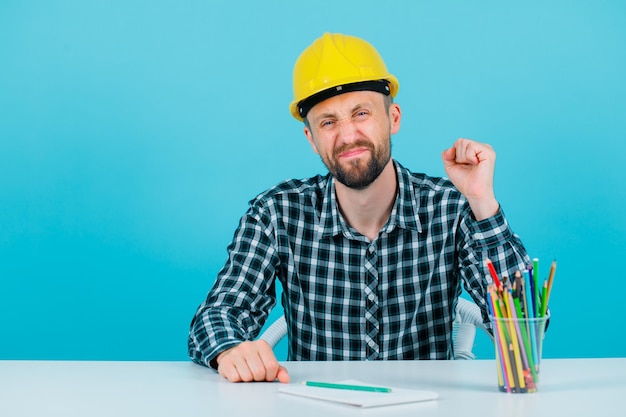 El joven ingeniero feliz está levantando el puño con fondo azul