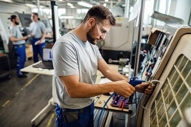 Joven ingeniero operando una máquina CNC en línea de producción en una fábrica